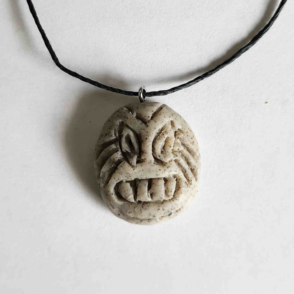 Handmade circular stone-textured ceramic pendant with a carved Taíno ancestral face petroglyph on a black cord necklace, inspired by indigenous Caribbean rock art.