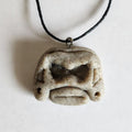 Handmade stone-textured ceramic pendant featuring a carved Taíno ancestral spirit face with deep eyes and traditional ears with holes on a black cord necklace, inspired by indigenous Puerto Rican petroglyphs.