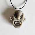 Handmade Arawak Taíno polymer clay face pendant necklace on black cord. Cream speckled sculpted indigenous Caribbean spirit face with bold features.