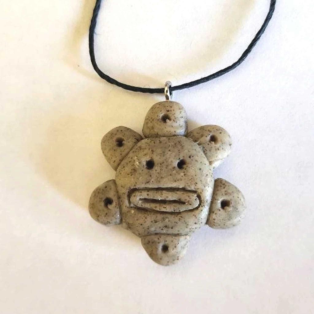 Handmade stone-textured ceramic pendant featuring the Taíno Sun God petroglyph on a black cord necklace, inspired by Puerto Rican indigenous art.