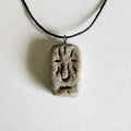 Handmade rectangular stone-textured ceramic pendant with a carved Taíno ancestral face petroglyph on a black cord necklace, inspired by indigenous Caribbean art.