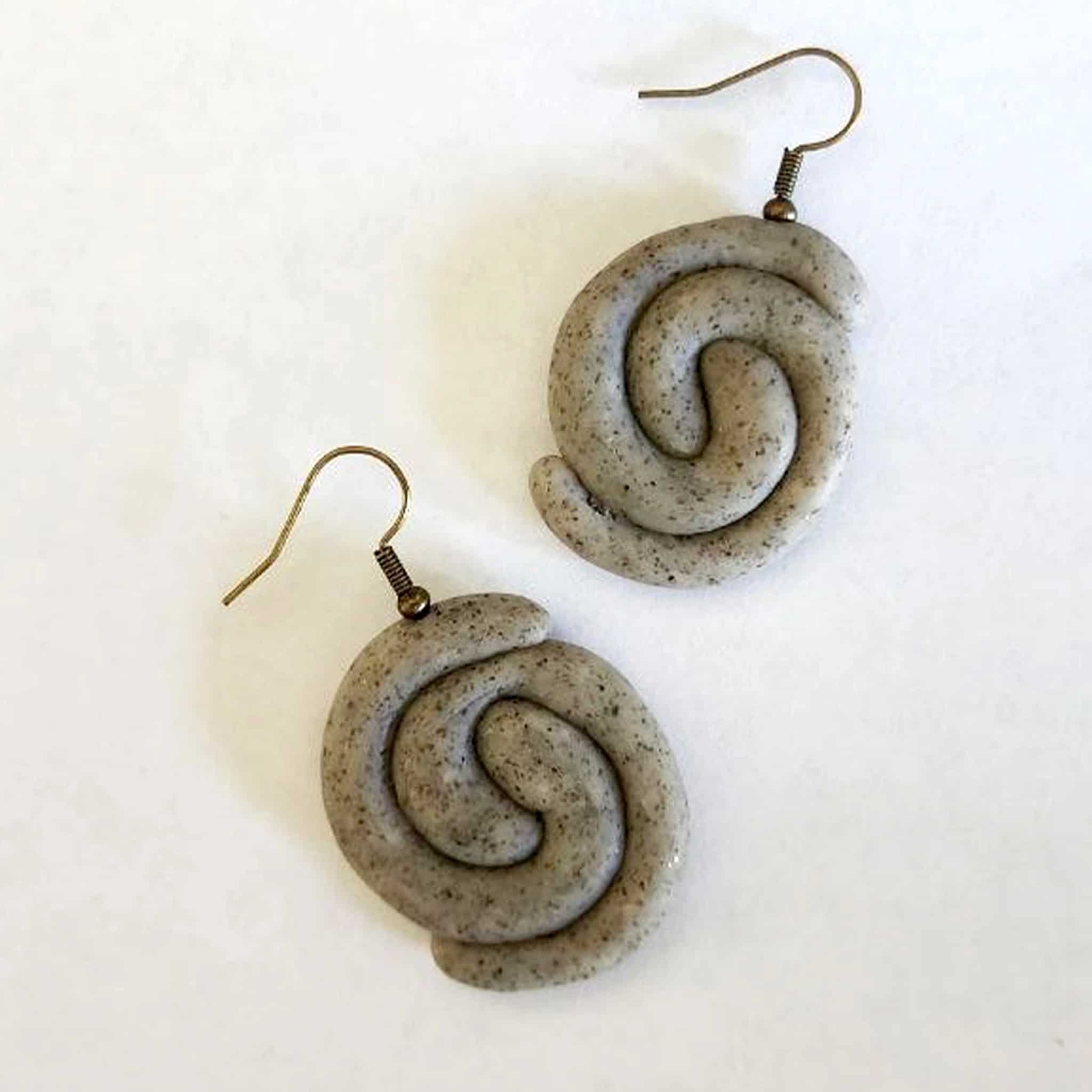 Handmade stone-textured ceramic earrings featuring a double spiral Taíno petroglyph representing water, hanging from bronze-tone hooks, inspired by Puerto Rican indigenous art.