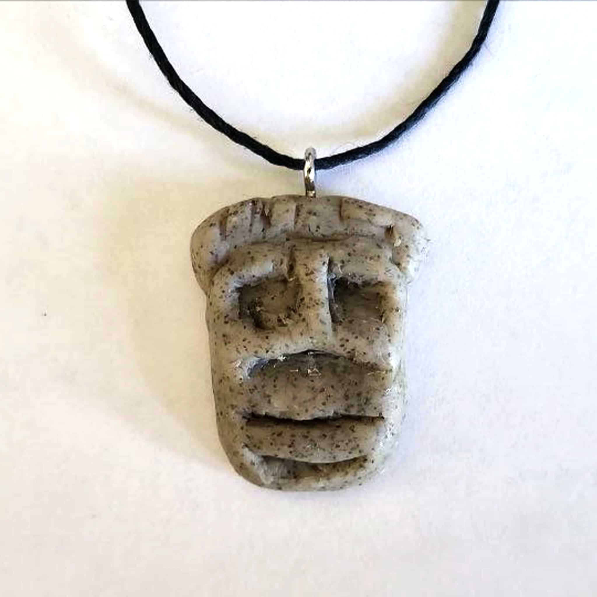 Handmade stone-textured ceramic pendant featuring a carved Taíno Zemi ancestral spirit face on a black cord necklace, inspired by Puerto Rican indigenous art.